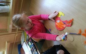 Emilia ozdabia papierowego ptaka podczas zajęć plastycznych