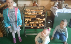 troje dzieci przy regale piekarniczym z wypieczonymi warkoczami chlebowymi
