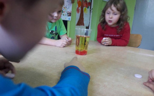 Dzieci obserwują dwukolorową  ciecz w kubku na stole