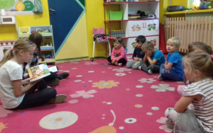 Uczennice szkoły czytają książkę, przedszkolaki uwaznie słuchają