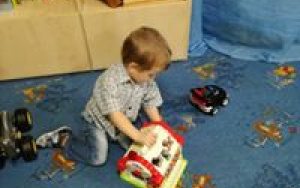Chłopiec bawi sie plastikową zabawką na dywanie