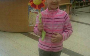 dziewczynka stoi,trzymaw ręce papierowego kwiatka