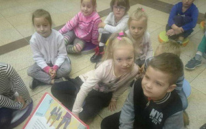 dzieci siedzą na podłodze,słuchają czytanej książki