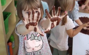 dzieci malują misia, dziewczynka z podniesionymi do góry rączkami brudnymi od farby