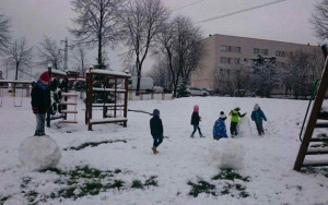 dzieci bawią się na śniegu, toczą kule, chłopiec stoi na jednej z nich