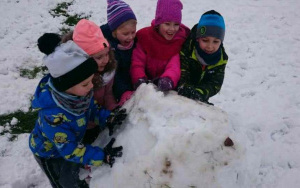 Piatka dzieci z radością i duzym wysiłkiem lepi ogromną, śniegową kulę