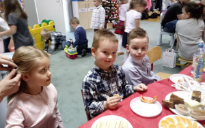 dwóch chłopców i dziewczynka przy stole z apetytem zajadają ciasto