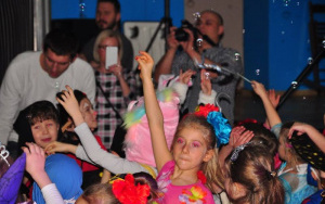 dziewczynka z uniesioną do góry ręką tańczy, wokół bawią się inne dzieci