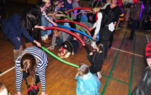 dzieci i dorośli w kostiumach przechodząpod tunelem z długich balonów
