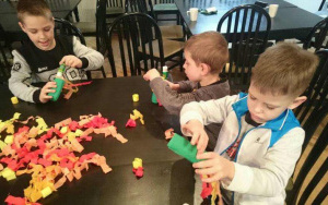 trzej chłopcy przy stole robią smogi - smoki z kolorowej bibuły i papierowych rolek 