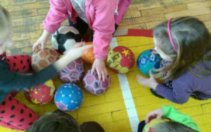 dzieci siedzą na dywanie z kolorowymi piłkami