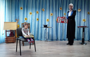 Dziewczynka na krzesełku trzymaksięgę, iluzjonista przekłada ramkę z cyframi