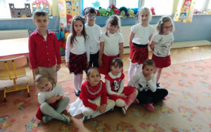 Grupa dzieci w biało - czerwonych strojach na dywanie