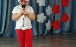 dziewczynka w białoczerwonym ubraniu i czapce z daszkiem mówi do mikrofonu