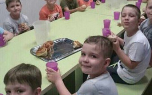 dzieci przy stole piją napój z fioletowych kubeczków, na talerzu słodkie bułki