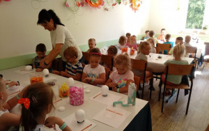 Dzieci przy stolikach, pani Sylwia rozdaje im turkusowe opaski na rękę