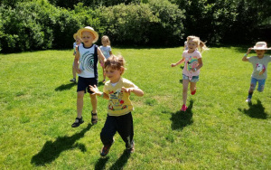 Kilkoro radosnych dzieci biegnie po zielonej trawie