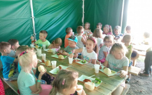 Przedszkolaki pod namiotem zajadają ze smakiem piknikowy obiad