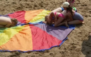 Dzieci na plaży przykucają na chuście animacyjnej