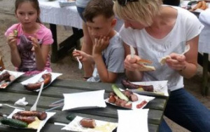 dzieci i rodzice przy drewnianych stołach zajadają kiełbaski