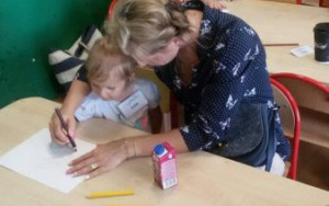 Dzieci z pomocą rodziców rysują przy stolikach