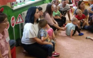 Dzieci wraz z rodzicami siedzą na dywanie razem z Panią Soliną