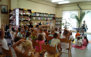 dzieci siedzą na matach i krzesłach,ręce wzniesione do góry - sygnalizują chęć odpowiedzi na pytanie