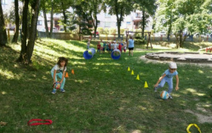 dzieci na trawie toczą piłkę slalomem pomiędzy kolorowymi palikami