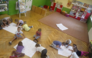 dzieci siedzą na podłodze nad arkuszami papierów,zaznaczają mazakami kolorowe punkty