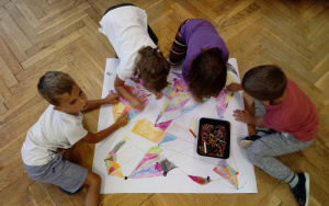 grupka dzieci pochylona nad arkuszem papieru koloruje mapę skarbów