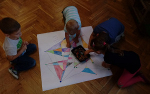 grupka dzieci pochylona nad arkuszem papieru koloruje mapę skarbów