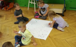 dzieci pochylone nad arkuszem papieru, zaznaczają mazakami kolorowe punkty i kreżlą linie