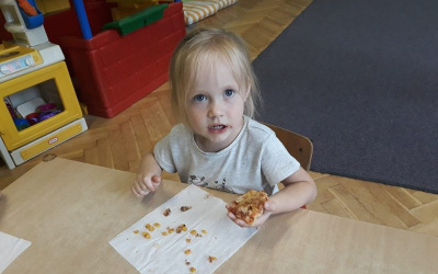 dziewczynka przy stoliku z kawałkiem pizzy w dłoni