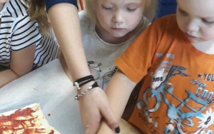 Chłopiec z pomocą Pani Martynki smaruje ciasto na pizzę sosem pomidorowym