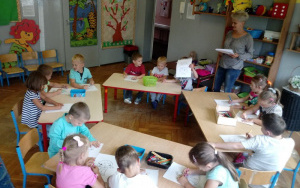 dzieci przy stolikach z kredkami,Pani Ania rozdaje kolorowanki