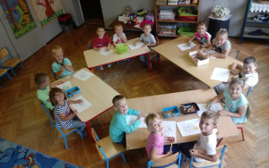uśmiechniete dzieci przy stolikach kolorują obrazki