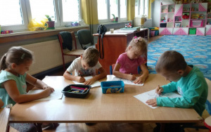 czwórka dzieci koloruje obrazki przy stoliku