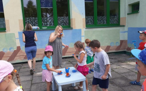 Dzieci i pani Agnieszka puszczają bańki mydlane za pomocą niebieskich kubeczków i dzbanka