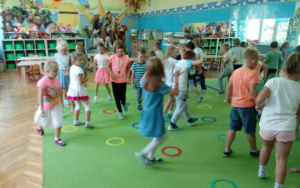 dzieci poruszają się swobodnie pomiędzy obręczami na dywanie w rytm muzyki