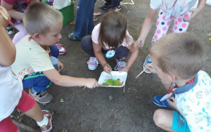 Dzieci mieszają farbę pędzelkami w pojemniku ustawionym na ziemi