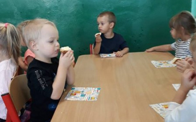 dzieci przy stolikach z apetytem  zajadają chałkę