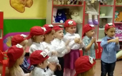 śpiewające dzieci w czerwonych czapeczkach klaszczą w dłonie