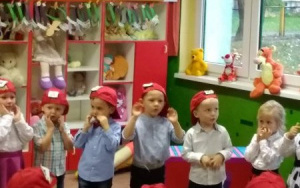 śpiewająca grupka dzieci w czerwonych czapeczkach, rączki zbliżone do policzków