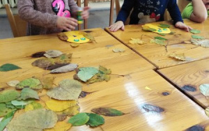 dzieci przy stole,na którym leżą suszone liściei owale zkolorowego brystolu. Wykonują sowy.
