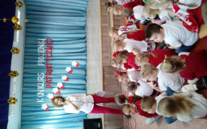Pani Renia w białoczerwonym stroju z mikrofonem zaprasza dzieci do rozpoczęcia uroczystości 