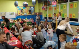 rodzice i dzieci przy stole z poczęstunkiem,pod sufitem unosząsię kolorowe balony