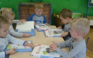 dzieci przy stolikach wykonują zadanie w książkach