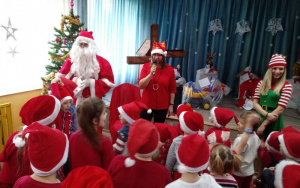 Pani Dyrektor rozmawia z Mikołajem i elfem, dzieci oczekują na prezenty