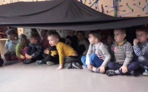 dzieci kulą się pod czarną, rozciągniętą nad podłogą płachtą