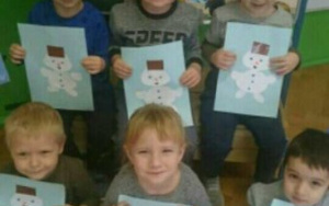 sześciu chłopcówprezentuje obrazki białych papierowych bałwanków na niebieskim tle